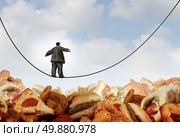 Overweight diet danger concept as an obese man walking on a tightrope high wire over mountains of greasy unhealthy junkfood as a metaphor for dieting risk and the challenges of eating disorders resulting in obesity. Стоковое фото, агентство Ingram Publishing / Фотобанк Лори