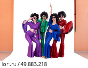 A group of girls in colorful flared suits and afro wigs pose in a photo studio. Disco style from the eighties or seventies. Стоковое фото, фотограф Лазаренко Светлана / Фотобанк Лори