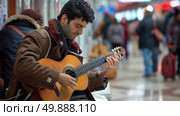 A man is seated on a bench, strumming a guitar with focused concentration. Стоковое AI-изображение, AI-художник Данила Большаков / Фотобанк Лори