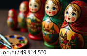 Traditional russian matryoshka dolls displayed on wooden surface with artistic palette and brushes. Стоковое AI-изображение, AI-художник Андрей Бакусов / Фотобанк Лори