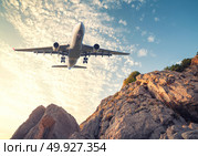 Big white aircraft is flying over rocks at sunset. Landscape with passenger airplane, mountains, colorful blue sky with clouds. Passenger airplane is landing. Business travel. Commercial plane. Стоковое фото, агентство Ingram Publishing / Фотобанк Лори