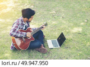 Young hipster man practiced guitar with laptop in the park,happy. Young hipster man practiced guitar with laptop in the park,happy and enjoy playing guitar. Стоковое фото, агентство Ingram Publishing / Фотобанк Лори