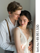 A young man and woman, dressed in vintage-inspired attire, share a close moment by a window bathed in gentle light. Стоковое AI-изображение, AI-художник Данила Большаков / Фотобанк Лори