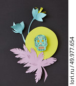 Decorative handcraft composition from paper with flowers, leaf and skull on a yellow round frame on black paper background, copy space. Calaveras attribute of the Mexican holiday of Calaca. Flat lay. Greeting card with Calaveras skull, decorated paper flowers calendula, leaf and creative on a yellow frame on a black paper. Стоковое фото, агентство Ingram Publishing / Фотобанк Лори