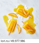Ice cream lolly with fresh peach slices. Pattern of ice cream splashes and pieces of ice gray marble background with space for text. Flat lay. Appetizing melting ice cream on a stick with a pattern of splashes of ice cubes and pieces of peach on a gray marble background copy space. Flat lay. Стоковое фото, агентство Ingram Publishing / Фотобанк Лори