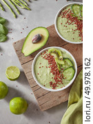 Vegetarian food smoothies from green organic vegetables with flax seeds and lime slices in a white bowl on a wooden board, served with a textile green towel on a grey background.. Top view of a green smoothie from avacado, cucumber, kiwi, asparagus with flax seeds and lime slices in a white bowl on a wooden board on a grey background. Стоковое фото, агентство Ingram Publishing / Фотобанк Лори