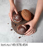 Homemade chocolate ice cream in a coconut shell with whole coconut holding womans hands on a gray concrete background with place for text. Summer dessert.. A girl hold two halfs of coconut with chocolate sorbet with coconut chips and chocolate balls on a wooden board on a gray concrete. Top view. Стоковое фото, агентство Ingram Publishing / Фотобанк Лори