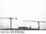 Industrial landscape with silhouettes of cranes on the gray cloudy background. Photo from the drone.. Building under construction with two tower cranes against a gray cloudy sky. Стоковое фото, агентство Ingram Publishing / Фотобанк Лори