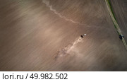 Aerial view plowing the spring field with a tractor, the post drank dragging behind the tractor. On the right side, a dirt road with a parked coarse. Ukraine. Photo from the drone. Aerial view the tractor plows the spring field.spring season of agricultural works at farmlands. Drone photograph. Стоковое фото, агентство Ingram Publishing / Фотобанк Лори