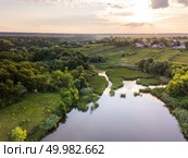 Aerial view from drone of countryside landscape with amazing natural greenery, fields and wild river on a summer sunset background.. Beautiful countryside landscape with village, forest, fields, river against summer cloudy sky at sunset. Стоковое фото, агентство Ingram Publishing / Фотобанк Лори
