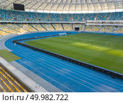 KIEV, UKRAINE - July 19, 2018. Panoramic view from drone of construction of the stadium roof, tribunes with yellow and blue seats of National Sports Complex Olimpiysky.. KYIV, UKRAINE - July 19, 2018. NSC Olimpiysky - the inside part with a football field, tribunes and treadmills. Редакционное фото, агентство Ingram Publishing / Фотобанк Лори