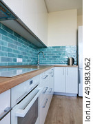 High glossy, white kitchen with blue tile, brown top, modern hob and oven. White glossy kitchen with modern appliances. Стоковое фото, агентство Ingram Publishing / Фотобанк Лори