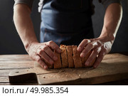 Wholegrain bread with wheat grains on rustic wooden background with man heands. Healthy eating concept. Baker man holding a healthy slice bread on a wooden board. Стоковое фото, агентство Ingram Publishing / Фотобанк Лори