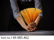 Woman’s hands with gluten free spaghetti made from rice and maize over a wooden table on a black background. Mediterranean healthy diet. Fresh italian uncooked homemade pasta in female hands over a wooden table. Стоковое фото, агентство Ingram Publishing / Фотобанк Лори