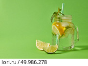 Glass jar on a green table with homemade sparkling non-alcoholic beverage with plastic straw on a green background. Concept of cold alcoholic or non-alcoholic summer drinks.. Refreshing cold non-alcoholic drink in glass jar with ice cubes, slices of lime and lemon, sprig of mint with plastic straw on a green background. Copy space. Стоковое фото, агентство Ingram Publishing / Фотобанк Лори