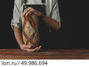 Men’s hands holding fresh warm bread on the background , tonned photo. Baker’s hands hold an oval bread. Стоковое фото, агентство Ingram Publishing / Фотобанк Лори