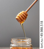 Sweet flower natural honey dripping into a jar and wooden spoon on a gray concrete background, copy space. Jewish rosh hashanah holiday concept.. Dripping meadow organic natural honey from wooden dipper into a pot on a gray backgroun, pure raw sweet goodness. Стоковое фото, агентство Ingram Publishing / Фотобанк Лори