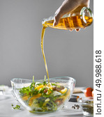 On the kitchen table was a bowl with a healthy salad. A woman’s hand pours oil into a salad on a gray background with a copy space.. A girl’s hand pours oil into a freshly prepared vegetable salad in a bowl on a gray background with copy space. Healthy food. Стоковое фото, агентство Ingram Publishing / Фотобанк Лори