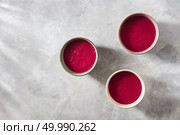 Ceramic handmade bowls with useful red smoothies for breakfast on a concrete background with shadows and space for text, flat lay. The concept of the healthy breakfasts and vegetarians. Three bowls with red beet smoothies on a concrete background, flat lay. Стоковое фото, агентство Ingram Publishing / Фотобанк Лори