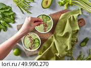 Green detox smoothies from avocado, spinach, kiwi, cucumber in a plate on a gray concrete background. A woman’s hand puts flax seeds on a plate. Healthy diet food. Top view. A woman’s hand puts flax seeds in a vitamin vegetable smoothie on a wooden board on a gray concrete background. Top view. Стоковое фото, агентство Ingram Publishing / Фотобанк Лори