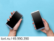 The hand of the girl and the man hold modern mobile phones on a blue background with copy space for text. Flat lay. Hand of a man and woman holding a mobile on a blue background with space for text. Modern technologies. Flat lay. Стоковое фото, агентство Ingram Publishing / Фотобанк Лори
