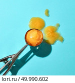 Creative composition from a ball of yellow ice cream on a metal spoon on a blue glass background with shadows. Food modern style.. Flat lay of a spoon for ice cream with yellow mango dessert and melted ice cream on a blue background with hard shadows. Стоковое фото, агентство Ingram Publishing / Фотобанк Лори