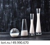 The glasses with dairy product milk standing on a black wooden table on a black background with copy space. Natural organic dairy product.. Preservation technology of natural organic dairy product milk in a glass bottles different shapes on a black wooden table. Стоковое фото, агентство Ingram Publishing / Фотобанк Лори