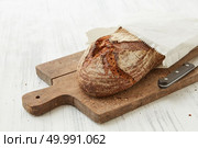 Isolated on white background of bread in a piece of paper on a cutting board with a knife. Fresh oval organic bread. Стоковое фото, агентство Ingram Publishing / Фотобанк Лори