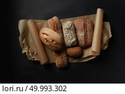 Mix fresh bread on parchment on black background in still life.. Assortment of different types of bread. Стоковое фото, агентство Ingram Publishing / Фотобанк Лори