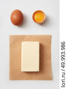 Top view of butter block on paper with raw chicken eggs over white background. Butter and eggs. Стоковое фото, агентство Ingram Publishing / Фотобанк Лори