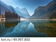Majestic mountains reflected in water in beautiful Dobbiaco lake at sunny morning in autumn.  Fall in Dolomites, Italy. Landscape with hills, trees, blue water and bright sunlight at sunrise. Nature. Стоковое фото, агентство Ingram Publishing / Фотобанк Лори