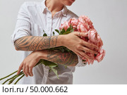 Girl with a tattoo on her hands, holding a bouquet of beautiful pink media roses on a gray background. Mothers Day. girl with a bouquet of flowers mother’s day. Стоковое фото, агентство Ingram Publishing / Фотобанк Лори