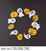 Round creative frame of colorful paper with handmade laughing flying ghosts, spirits, scary pumpkins on a black background, place for text. Halloween concept. Flat lay.. Decorative frame from round flying floating handcrafted ghost spirit and smiling yellow pumpkins on a black paper background. Стоковое фото, агентство Ingram Publishing / Фотобанк Лори