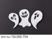 Decorative application from flying singing ghosts and spirit, smiling on a black paper background, place under text. Halloween concept. Top view.. Halloween party card with paper handmade laughing flying scary specters, spirits on a black background. Стоковое фото, агентство Ingram Publishing / Фотобанк Лори