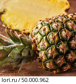 Closeup juicy half and whole of pineapple with green leaves on a wooden board on the kitchen table. Vitamin Fruit.. Closeup of whole and half juicy healthy pineapple presented on a kitchen board on a wooden table. Ingredient for dessert or salad. Стоковое фото, агентство Ingram Publishing / Фотобанк Лори