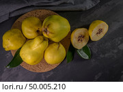 Ripe yellow quinces or queen apple fruits and sliced quince halves with seeds in craft cork plates on black rustic background. Стоковое фото, агентство Ingram Publishing / Фотобанк Лори