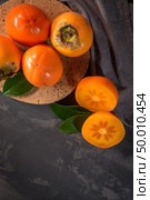 Ripe persimmon fruits in a cork plate on dark kitchen counter top. Стоковое фото, агентство Ingram Publishing / Фотобанк Лори