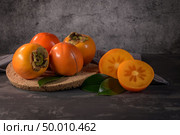 Ripe persimmon fruits in a cork plate on dark kitchen counter top. Стоковое фото, агентство Ingram Publishing / Фотобанк Лори