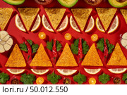 Creative geometric food pattern from mexican nachos corn chips, fresh vegetables, fruits, greens, chili, garlic - ingredients for tomato chili sauce on a red background. Flat lay. Ingredients of Guacamole dressing for mexican corn chips -chilly pepper, lemon slices, garlic, tomatoes, parsley green as a traditional pattern on a red background. Top view. Стоковое фото, агентство Ingram Publishing / Фотобанк Лори