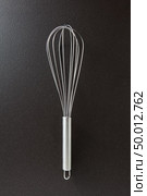 Metal whisk presented on a black concrete background with space for text.. Kitchen device for cooking different foods. Top view. Kitchen metal beater on a black concrete background with copy space. Kitchen appliance for cooking. Top view. Стоковое фото, агентство Ingram Publishing / Фотобанк Лори