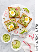 Toasts with avocado guacamole, fresh radish, boiled egg, chia and pumpkin seeds. Diet breakfast. Delicious and healthy plant-based food. Flat lay. Top view. Стоковое фото, агентство Ingram Publishing / Фотобанк Лори