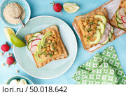 Toasts with chickpea hummus, avocado, fresh radish, cucumber, sesame seeds and flaxseed sprouts. Diet breakfast. Delicious and healthy plant-based vegetarian, vegan food. Flat lay. Top view. Стоковое фото, агентство Ingram Publishing / Фотобанк Лори