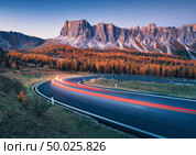 Blurred car headlights on winding asphalt road in mountains at sunset in autumn. Spectacular landscape with light trails, forest, rocks and purple sky at night in fall. Car driving on roadway. Стоковое фото, агентство Ingram Publishing / Фотобанк Лори
