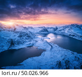 Aerial view of snowy mountains, sea, colorful cloudy sky at sunset in Lofoten islands, Norway. Winter landscape with snow covered rocks and seacoast and blue sky. Top view of Norwegian Fjords at dusk. Стоковое фото, агентство Ingram Publishing / Фотобанк Лори