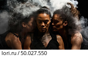 In a dimly lit setting, three women are closely huddled, with wisps of mist swirling around them, creating a dramatic and intimate atmosphere. Стоковое AI-изображение, AI-художник Данила Большаков / Фотобанк Лори