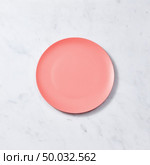 Decorative clay dish, covered with glazed in a color of the year 2019 Living Coral pantone on a gray background. Traditional ceramic handcrafted. Can be used for display or montage your products.. Porcelain handmade empty plate in a color of the year 2019 Living Coral pantone on a gray marble table, place for text. Flat lay. Стоковое фото, агентство Ingram Publishing / Фотобанк Лори