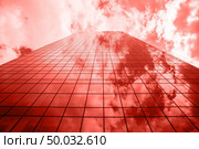 Perspective of urban glass business skyscraper with shadows and reflections of sky clouds on a shiny surface in a fashionable pantone trendy color of spring-summer 2019 season.. Glass facade of modern business building with reflections and shadows in a color of the year 2019 Living Coral pantone on a background oh cloudy sky. Стоковое фото, агентство Ingram Publishing / Фотобанк Лори