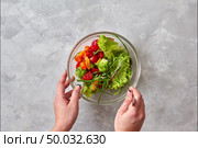 Woman hands cooking vegan salat from natural organic vegetables and greens, cheese, olive oil and eating fresh salad from glass bowls and white plate on a gray concrete background. Stop motion animation.. The process of preparing a healthy vegetarian salad from organic natural vegetables, greens, cheese, olive oil and eating of salad with female hands on a gray stone background. Flat lay. Стоковое фото, агентство Ingram Publishing / Фотобанк Лори