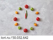 Vegetable clock from colorful cherry tomatoes, carrots, brussels cabbage and moving arrows from chili peppers on a gray stone background. Flat lay.. Moving colored vegetables make up a clock with moving arrows from chili pepper on a gray concrete background. Stop motion animation. Стоковое фото, агентство Ingram Publishing / Фотобанк Лори
