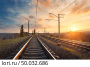 Railroad against beautiful sky at sunset. Industrial landscape with railway station, colorful blue sky with clouds, trees and green grass, yellow sunlight. Railway junction. Heavy industry. Travel. Стоковое фото, агентство Ingram Publishing / Фотобанк Лори